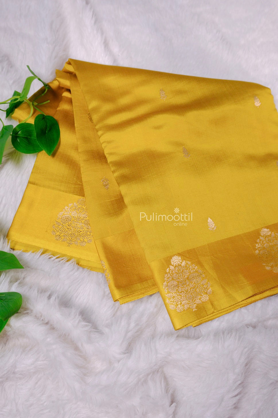 Mustard yellow Kerala silk saree with silver zari butta and temple motifs on pallu, displayed on white fur background.