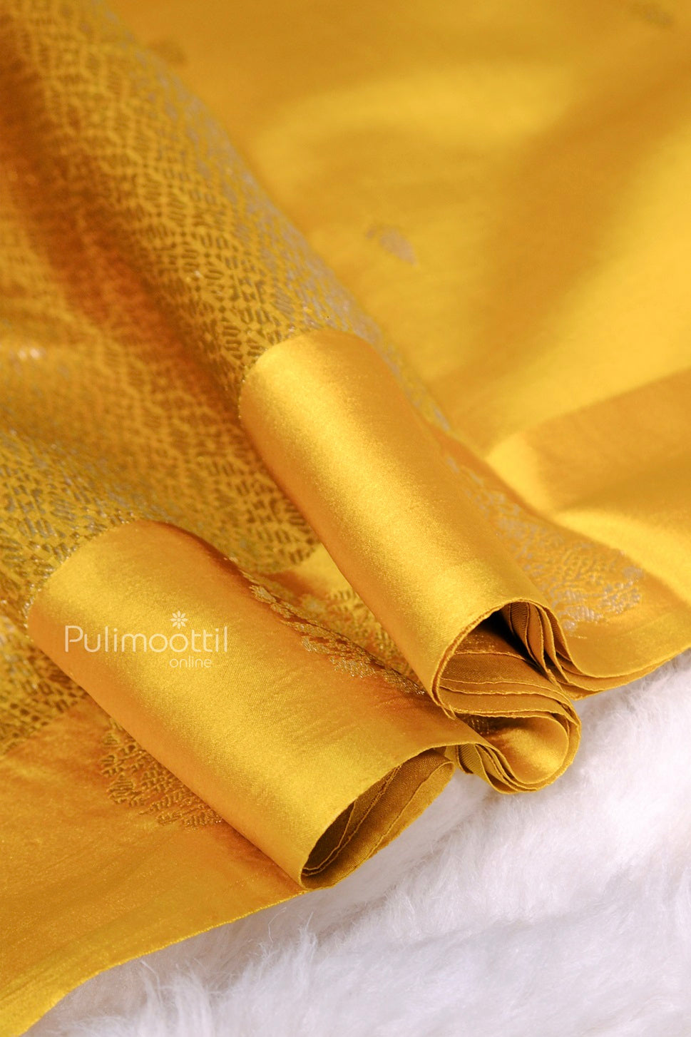 Close-up view of yellow silk saree showcasing lustrous texture and detailed zari work on pallu.