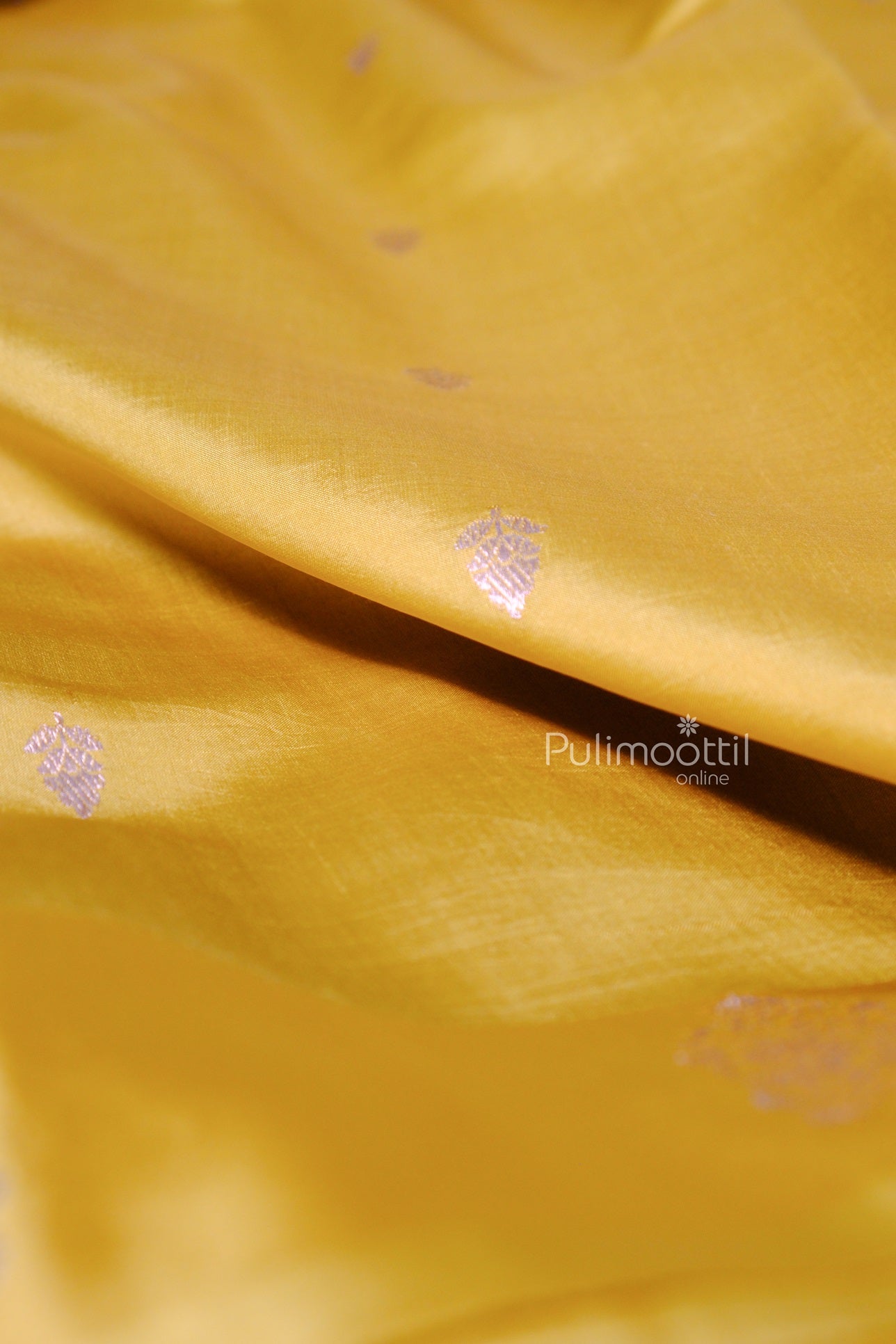 Smooth mustard yellow Kerala saree fabric with delicate silver motifs scattered across the body.