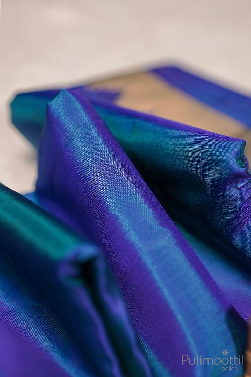 Close-up of peacock blue Kanchipuram saree blouse fabric with golden zari work.