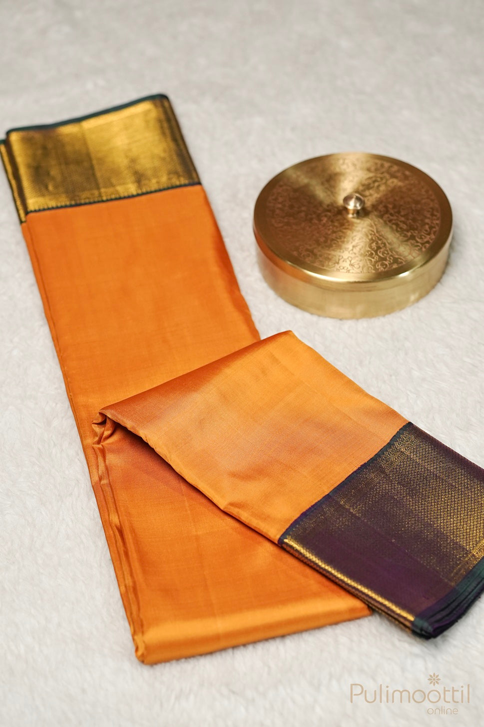 Mustard yellow Kanchipuram soft silk saree with a plain body, contrasting golden and purple borders, elegantly displayed alongside a decorative golden box on a soft white surface.