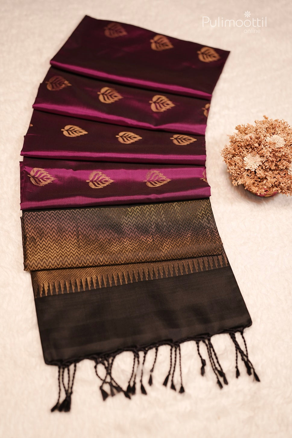 Close-up of dark pink Kanchipuram saree fabric showing golden leaf buttas and black border detail.