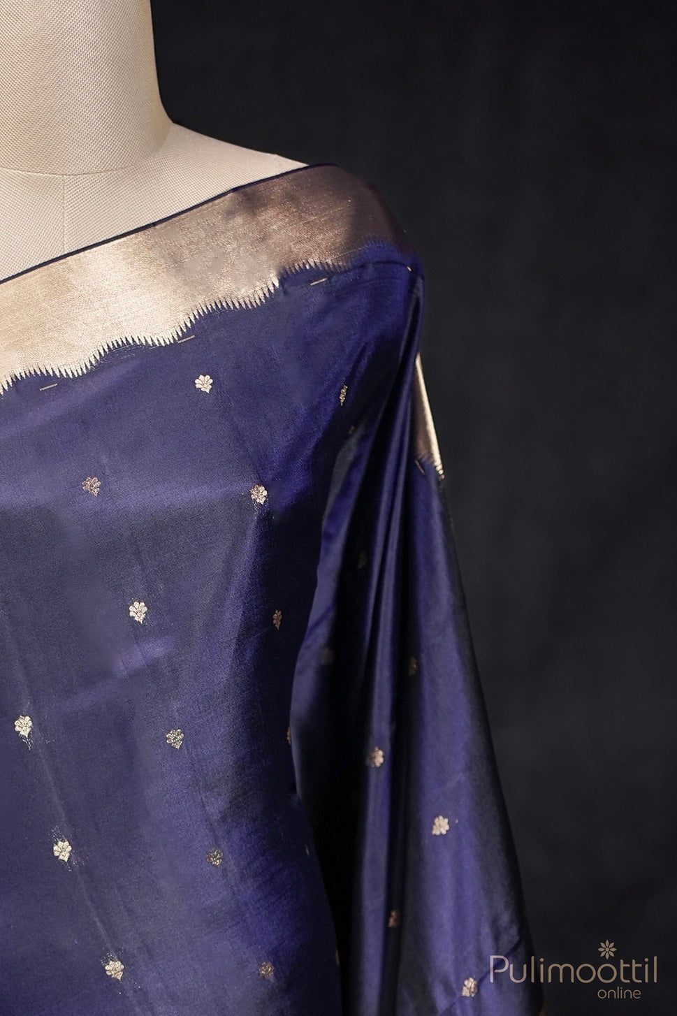 Close-up view of dark blue Kanchipuram silk saree with golden buttas and zari border on mannequin.
