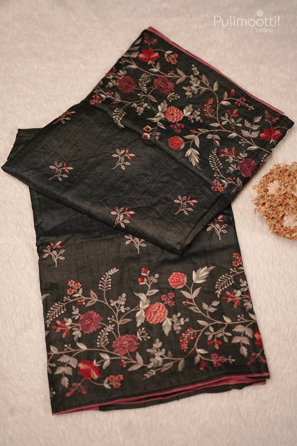 Folded black saree with red and white floral embroidery, featuring a contrasting pink piping along the edges.