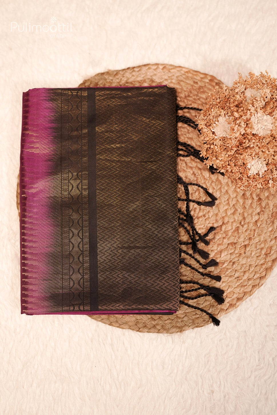 Folded dark pink Kanchipuram saree with golden leaf buttas and black zig zag design pallu with tassels, displayed on a white surface.
