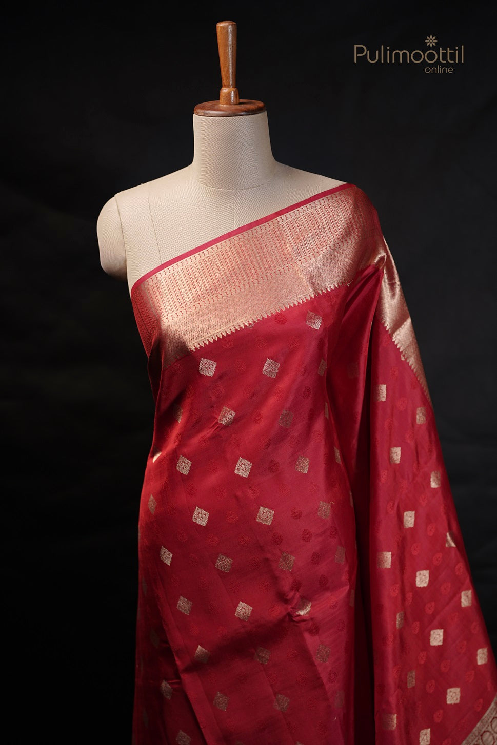 Chilli red Kanchipuram saree draped on a mannequin, showcasing golden buttas and designer border.
