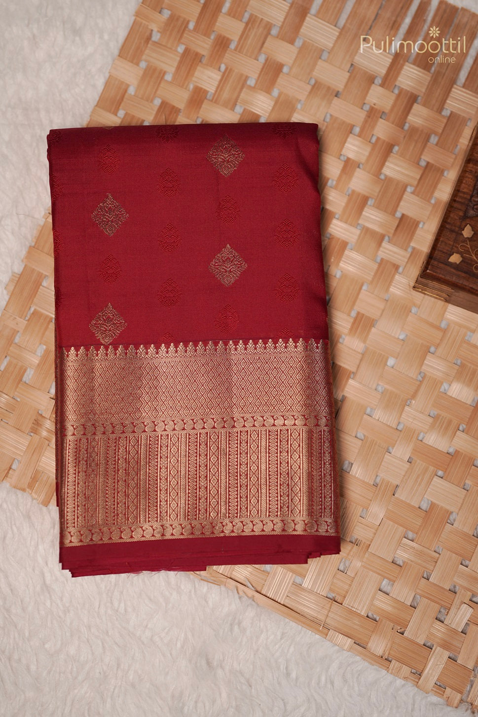 Folded chilli red Kanchipuram saree with golden buttas and intricate designer border placed on a white surface.