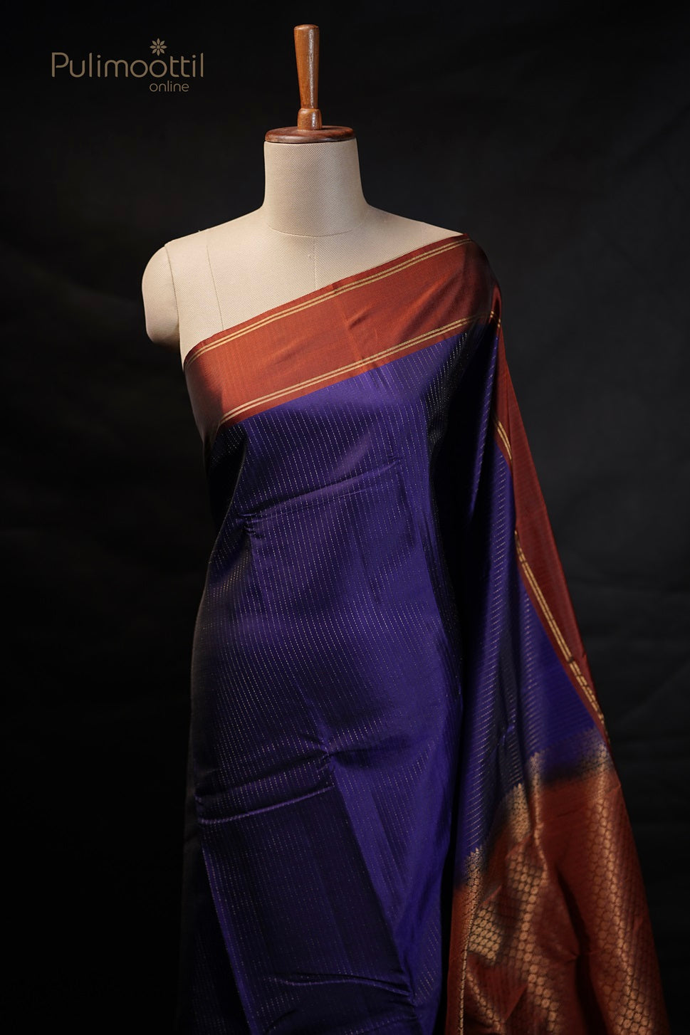Violet saree draped on a mannequin, showing golden stripes on the body and rust-colored border.