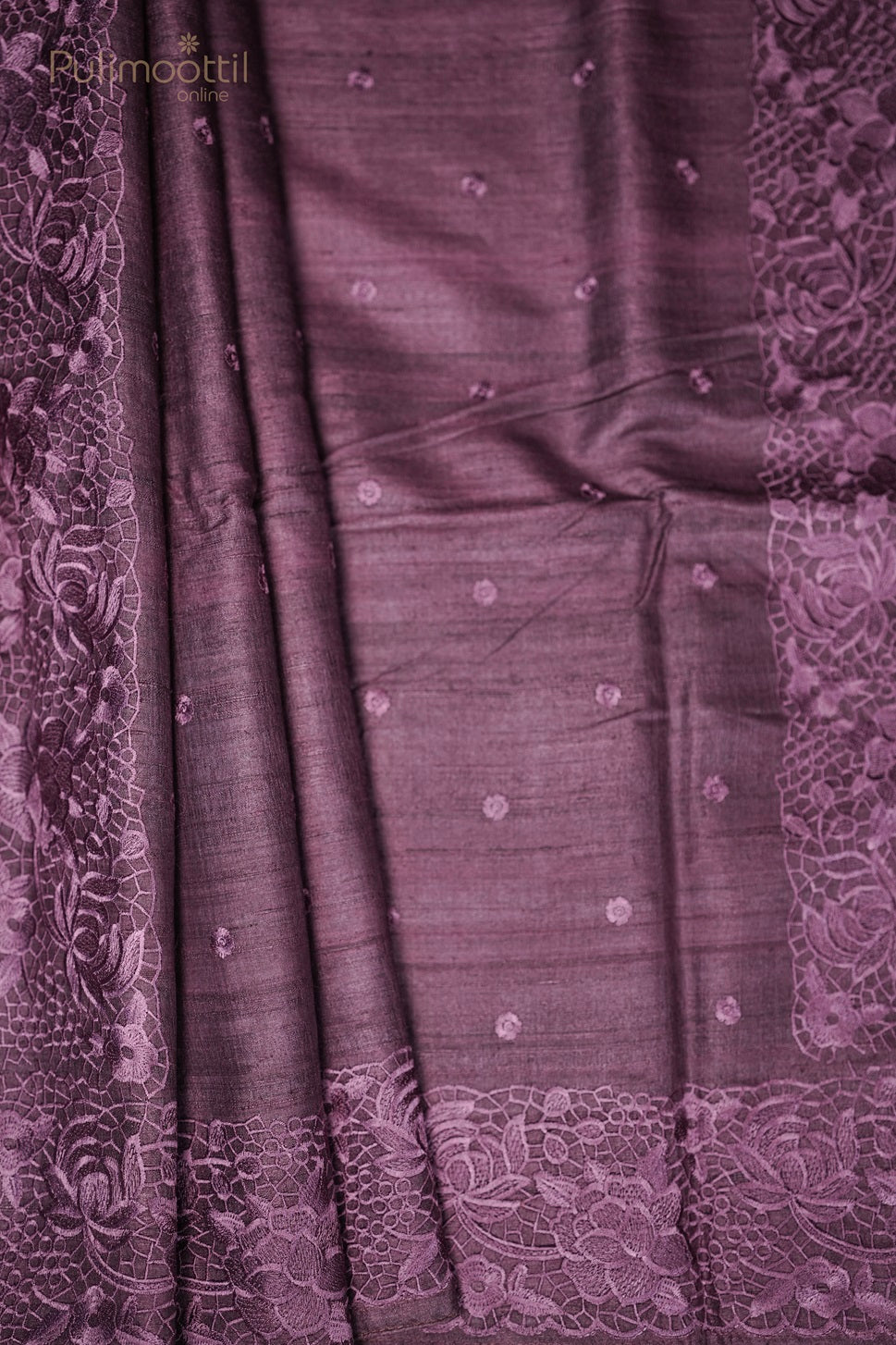Folded purple saree with floral lace border placed next to a dried flower arrangement.