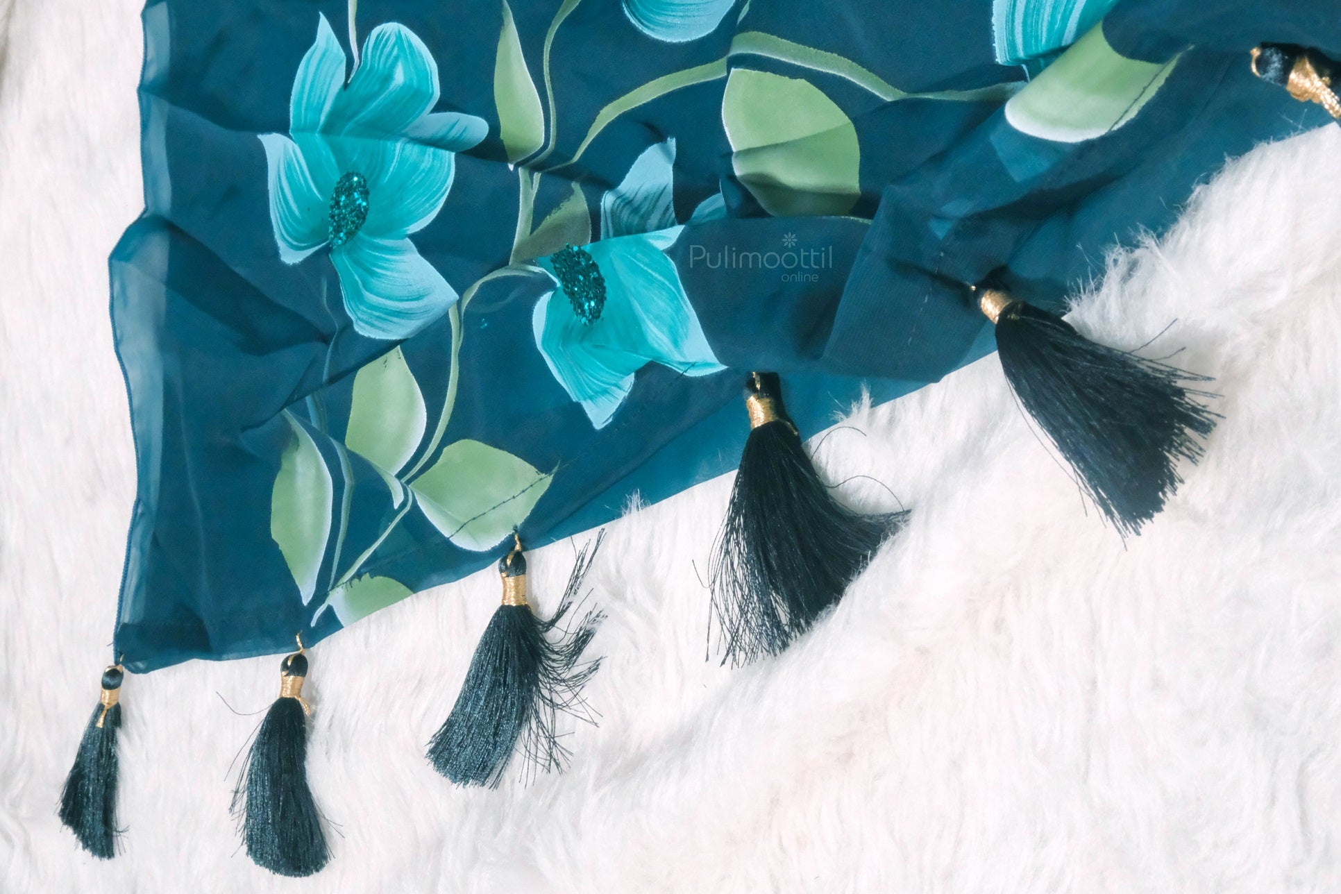 Peacock blue organza saree with floral patterns and elegant black tassels on the pallu