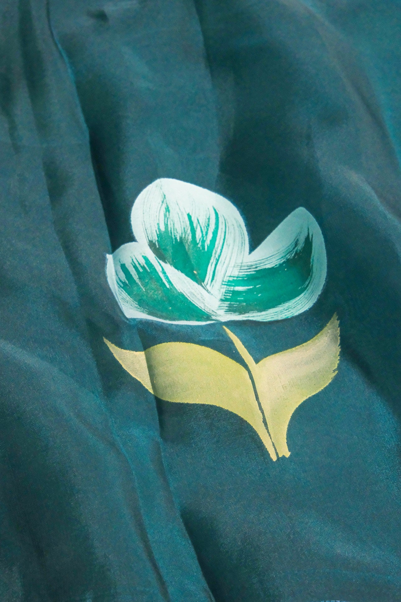 Close-up of hand-painted green floral motif on peacock blue organza fabric