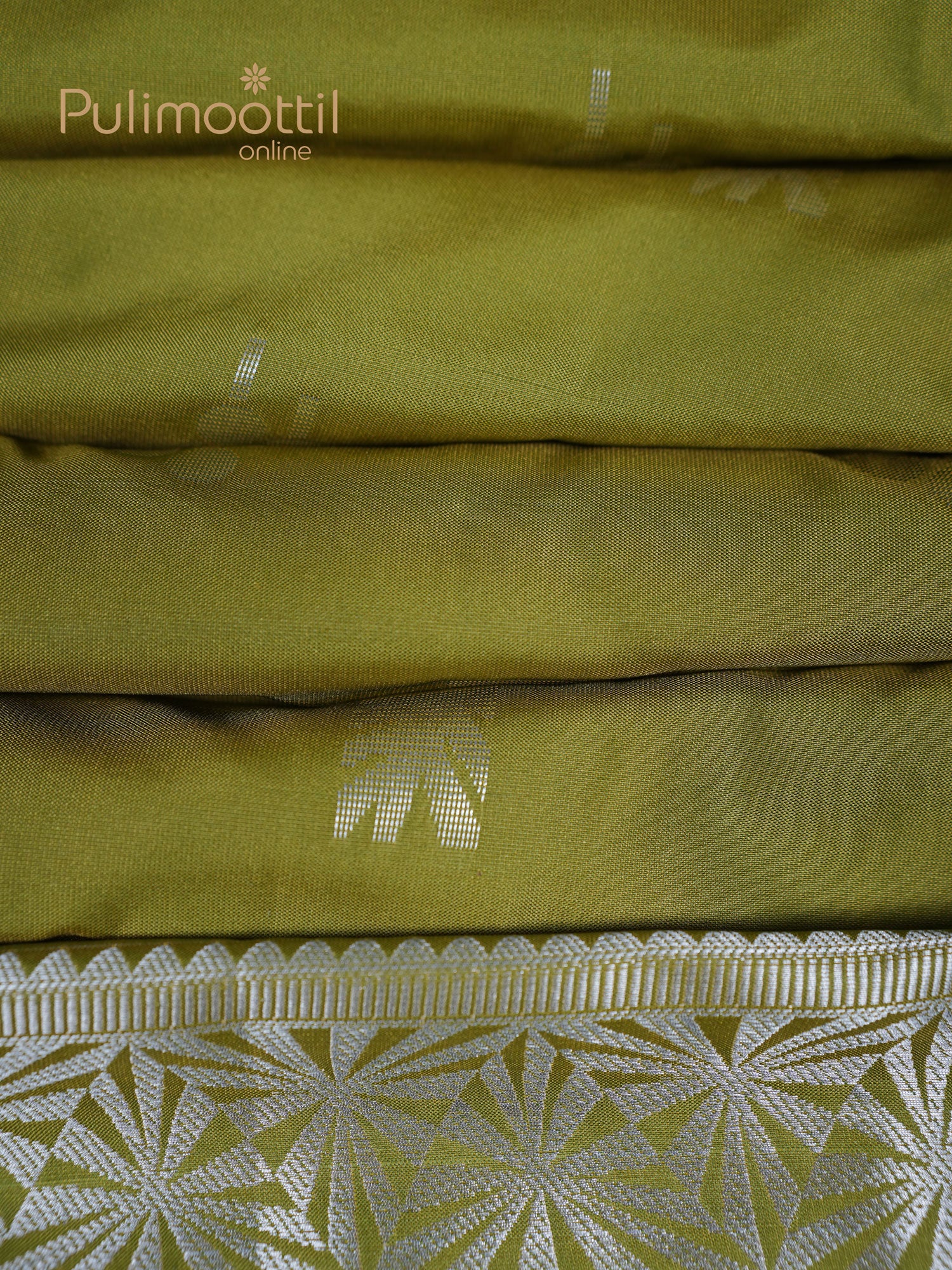 Olive-green semi-silk saree neatly folded to highlight the silver geometric border at the bottom, with subtle silver butta motifs visible across the body.