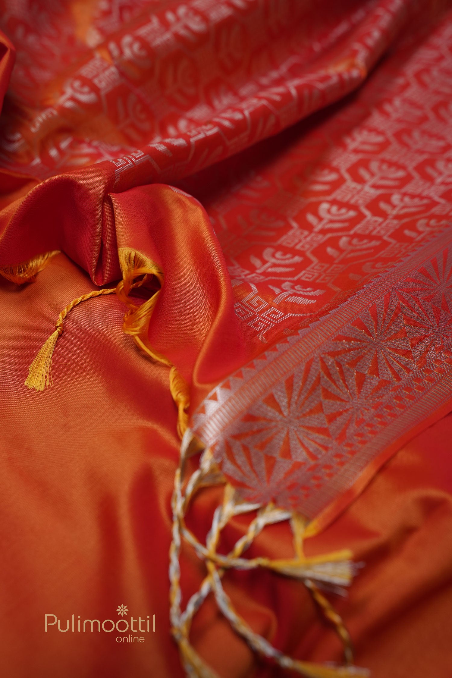 Bright red‑orange semi‑silk blouse piece featuring fine silver geometric and floral butta motifs, with a silver-patterned edge and yellow-gold twisted tassels.
