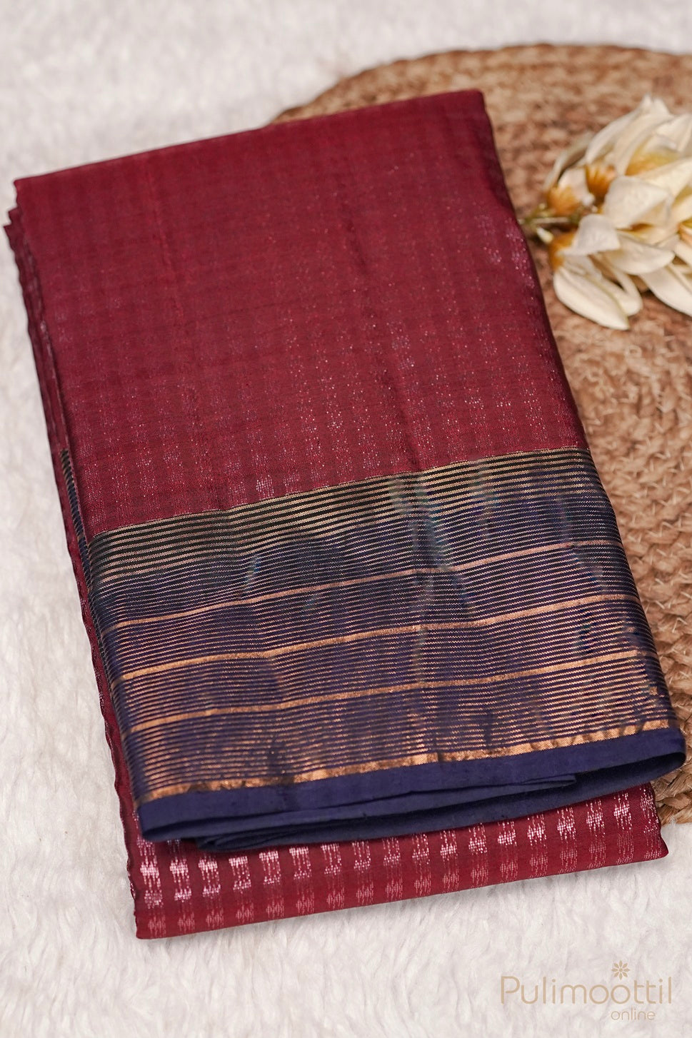 Folded maroon Kanchipuram designer saree with rose gold zari and contrasting blue border.
