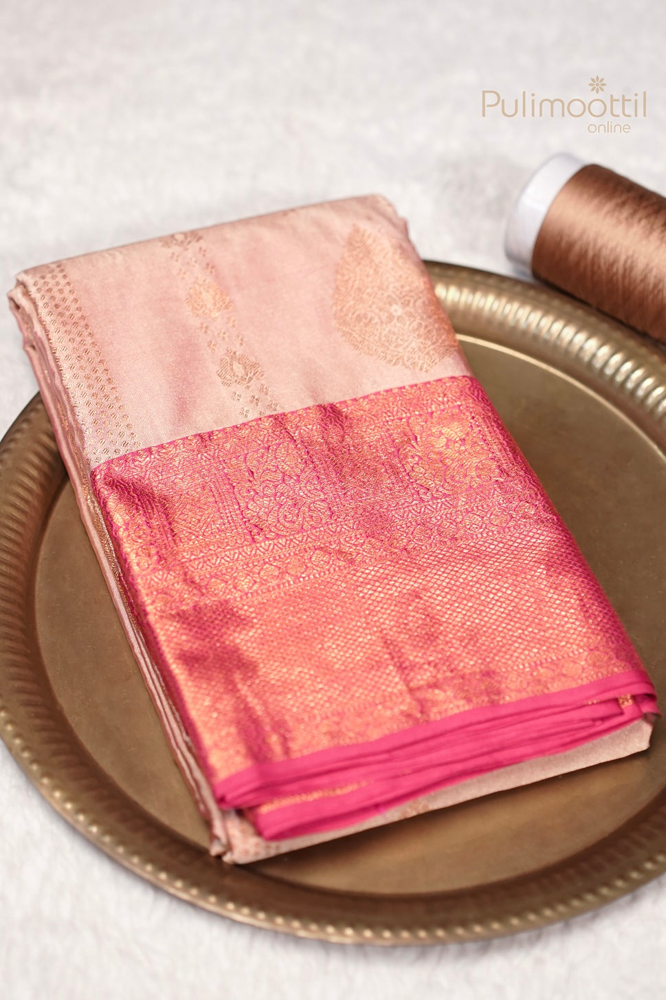 Melon colour semi Kanchipuram saree with designer body and contrast border neatly folded on a brass plate.
