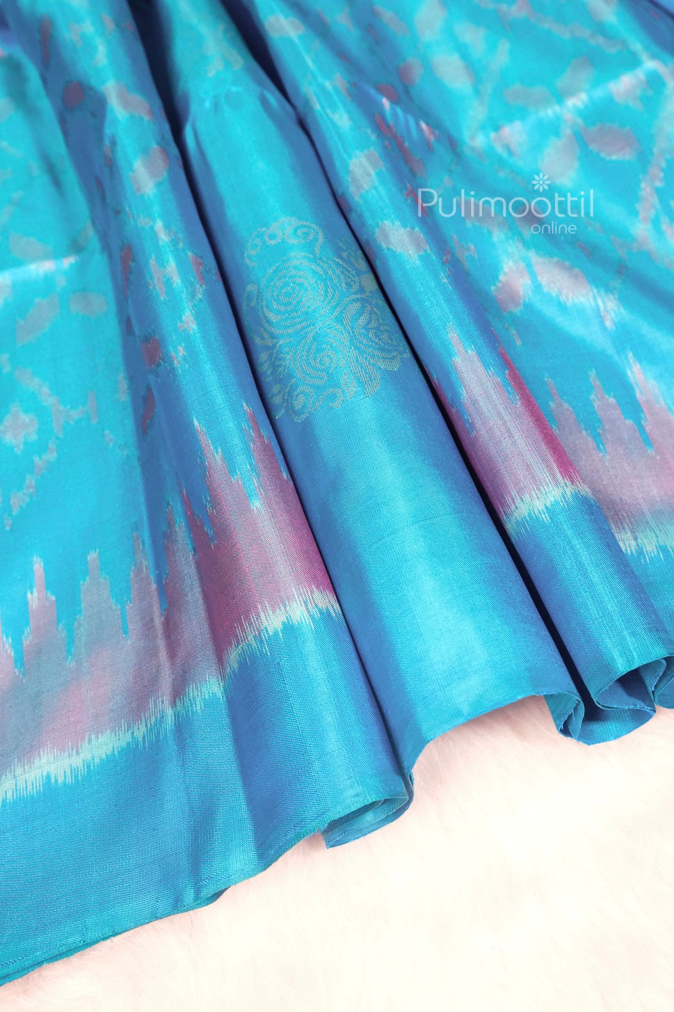 Close-up view of a vibrant turquoise blue Kanchipuram silk saree featuring subtle pink Ikat patterns and a delicate golden zari motif, ideal for weddings and festive occasions.