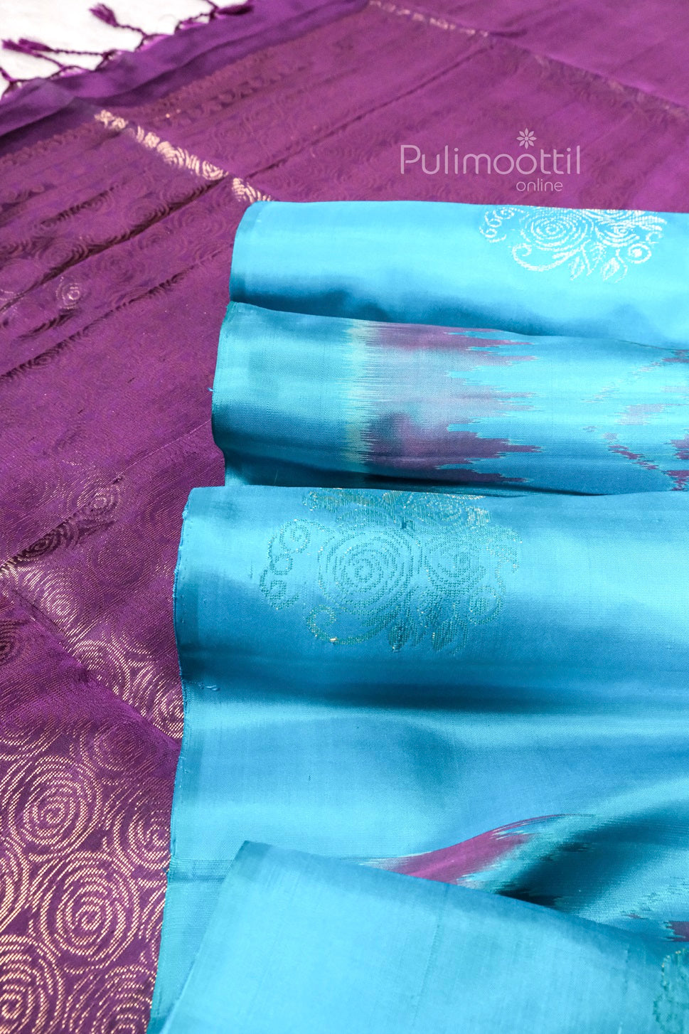 Aqua blue pure soft silk saree with subtle golden zari floral motifs and purple Ikat print, paired with a rich purple pallu featuring intricate golden zari design.