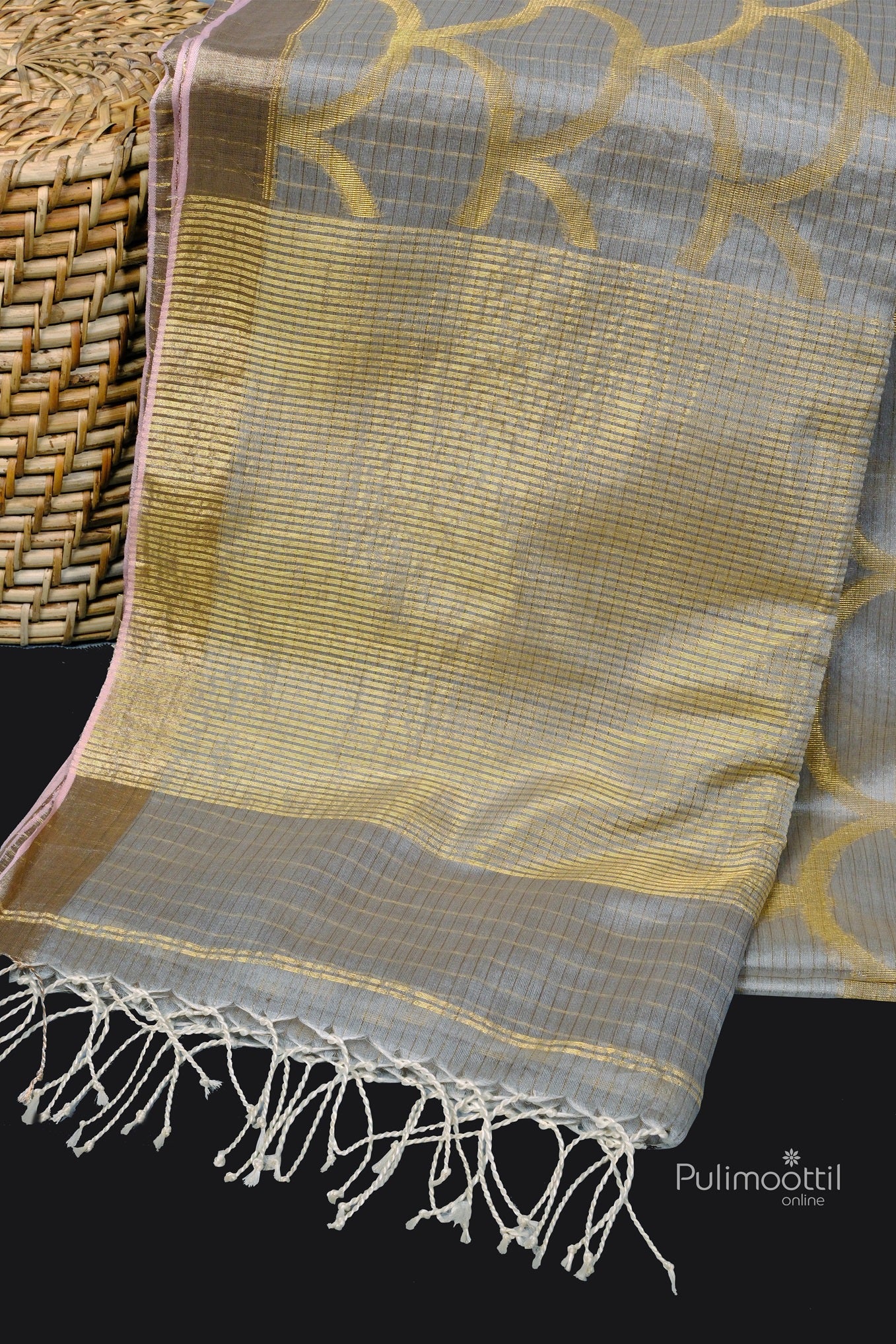 View of saree pallu with fine golden zari lines and tassels, laid beside a woven basket