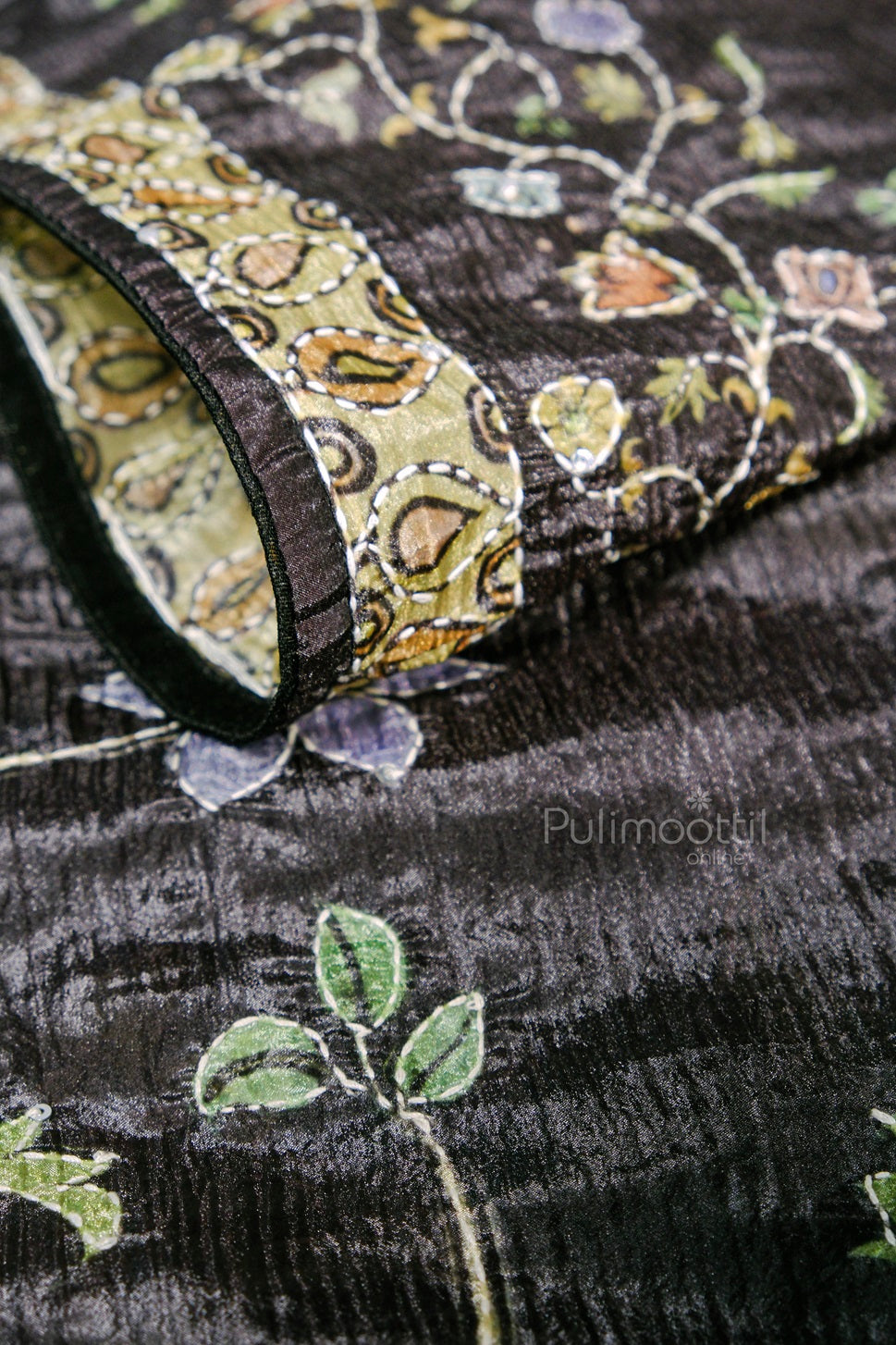  Close-up of a black silk saree with intricate multicolored floral embroidery and a contrasting printed border in olive and beige.