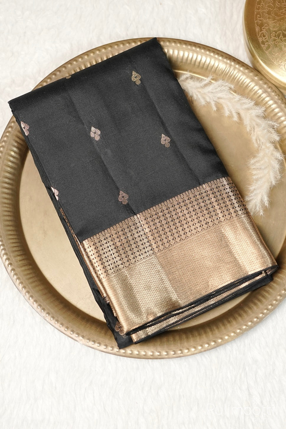 Black Kanchipuram soft silk saree with golden buttas and rich designer zari border placed on a brass plate