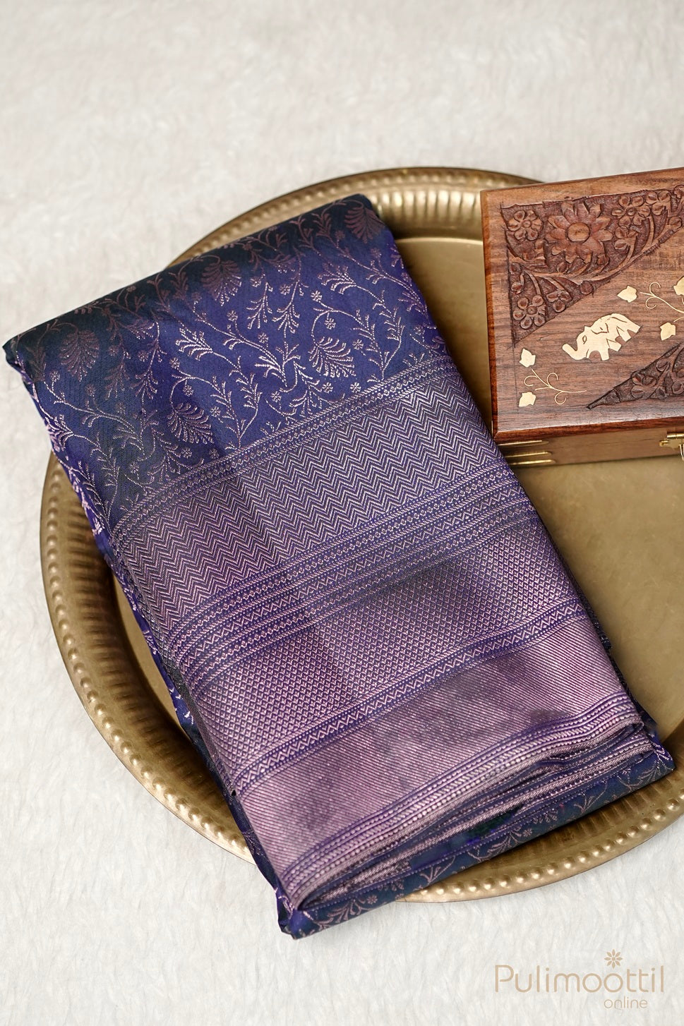 Folded deep blue Kanchipuram brocade saree with rose gold zari motifs and ornate designer border.