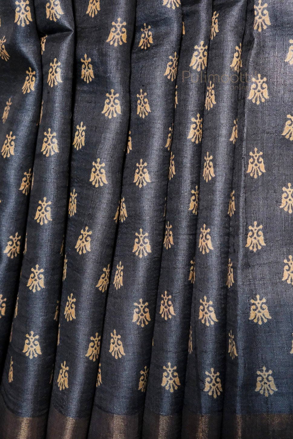 Black cotton silk fabric with golden traditional motifs and zari detailing, neatly pleated to highlight the intricate butti design.