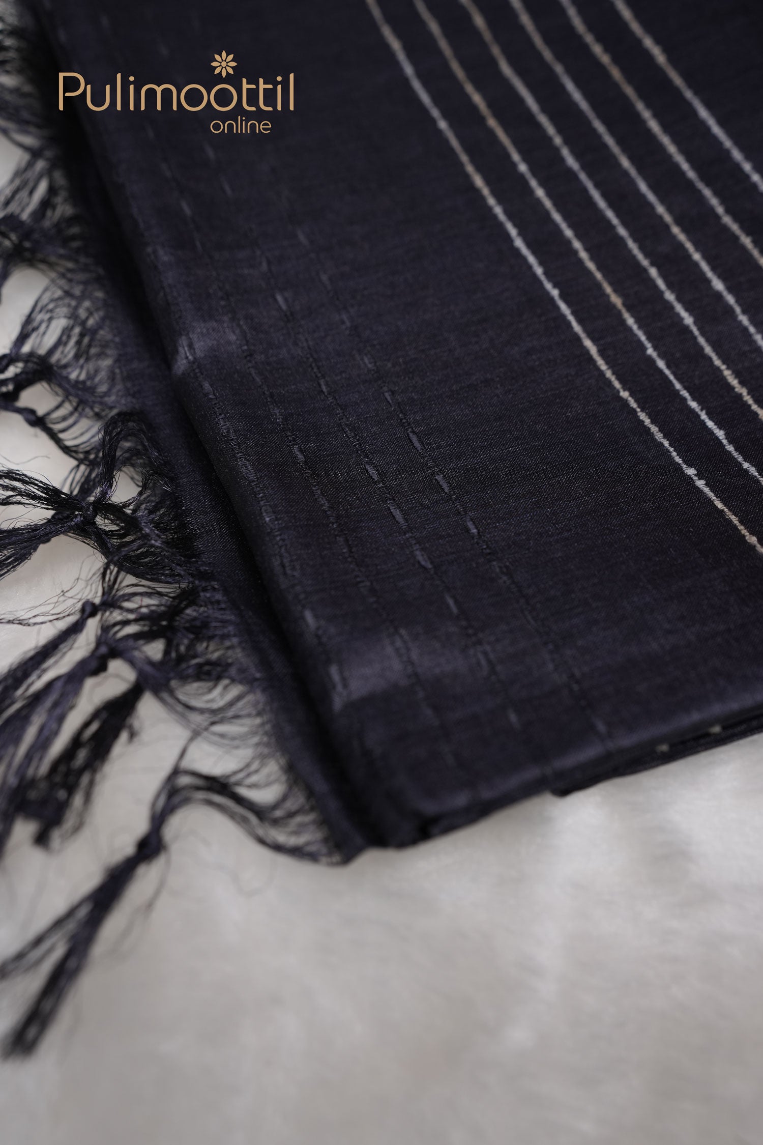 Folded charcoal black Tussar silk saree with visible tassels, showcasing its soft texture and minimalist self-thread design.