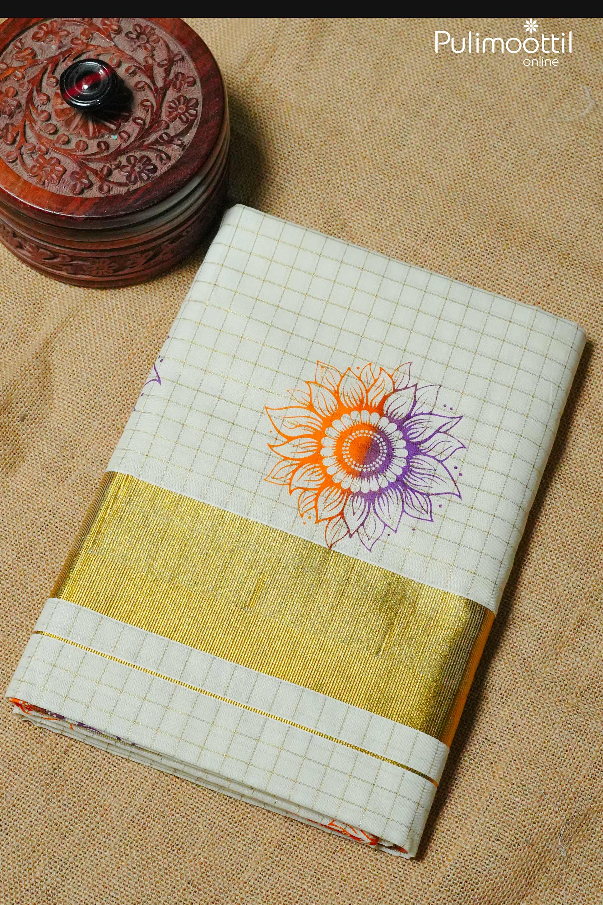 Folded cream Kerala kasavu saree with golden zari border and orange-purple floral motif, placed on jute background – perfect for Onam celebrations.