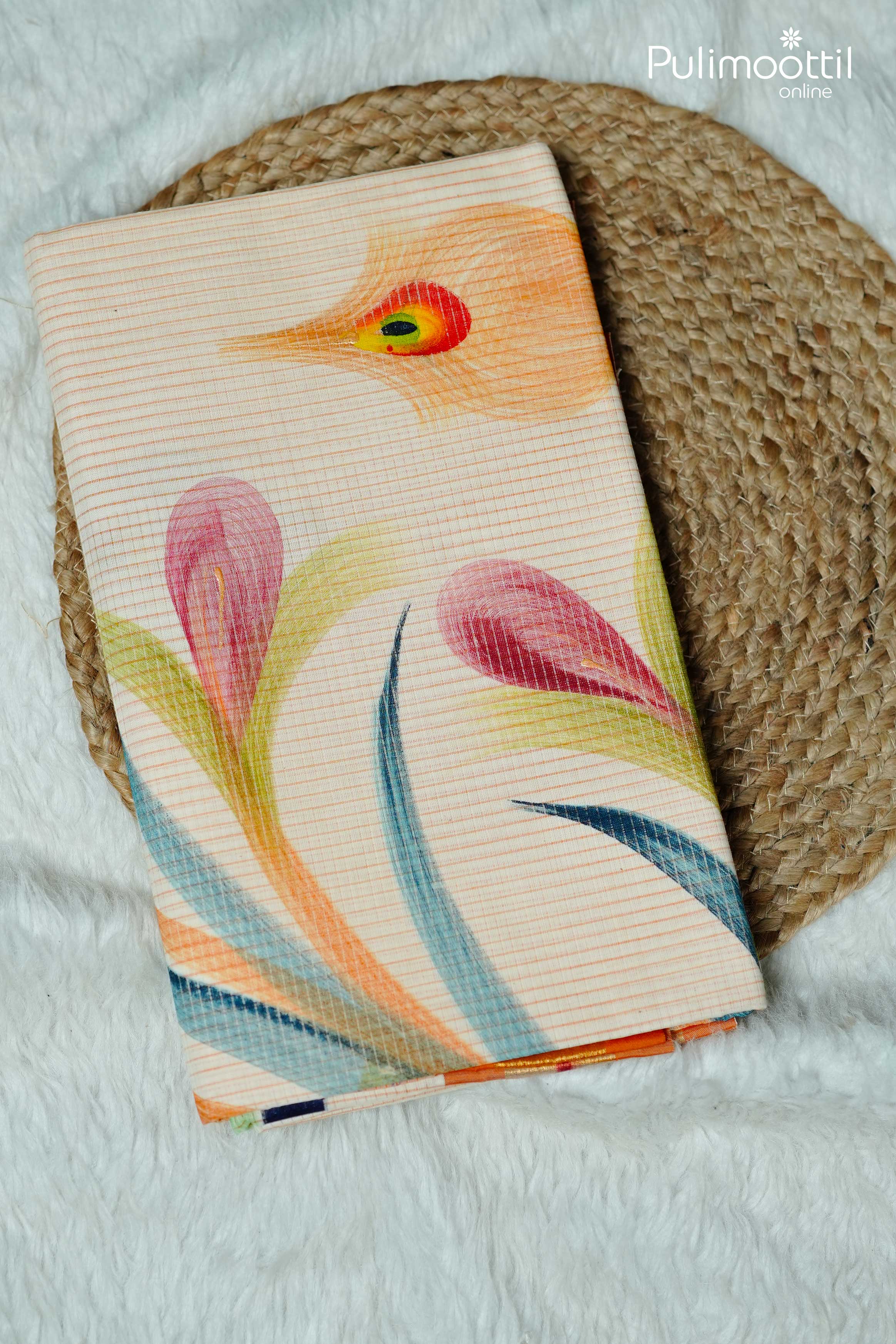 Folded cream Kerala tissue saree with multicolor peacock feather and floral motifs, placed on woven mat over white textured fabric.