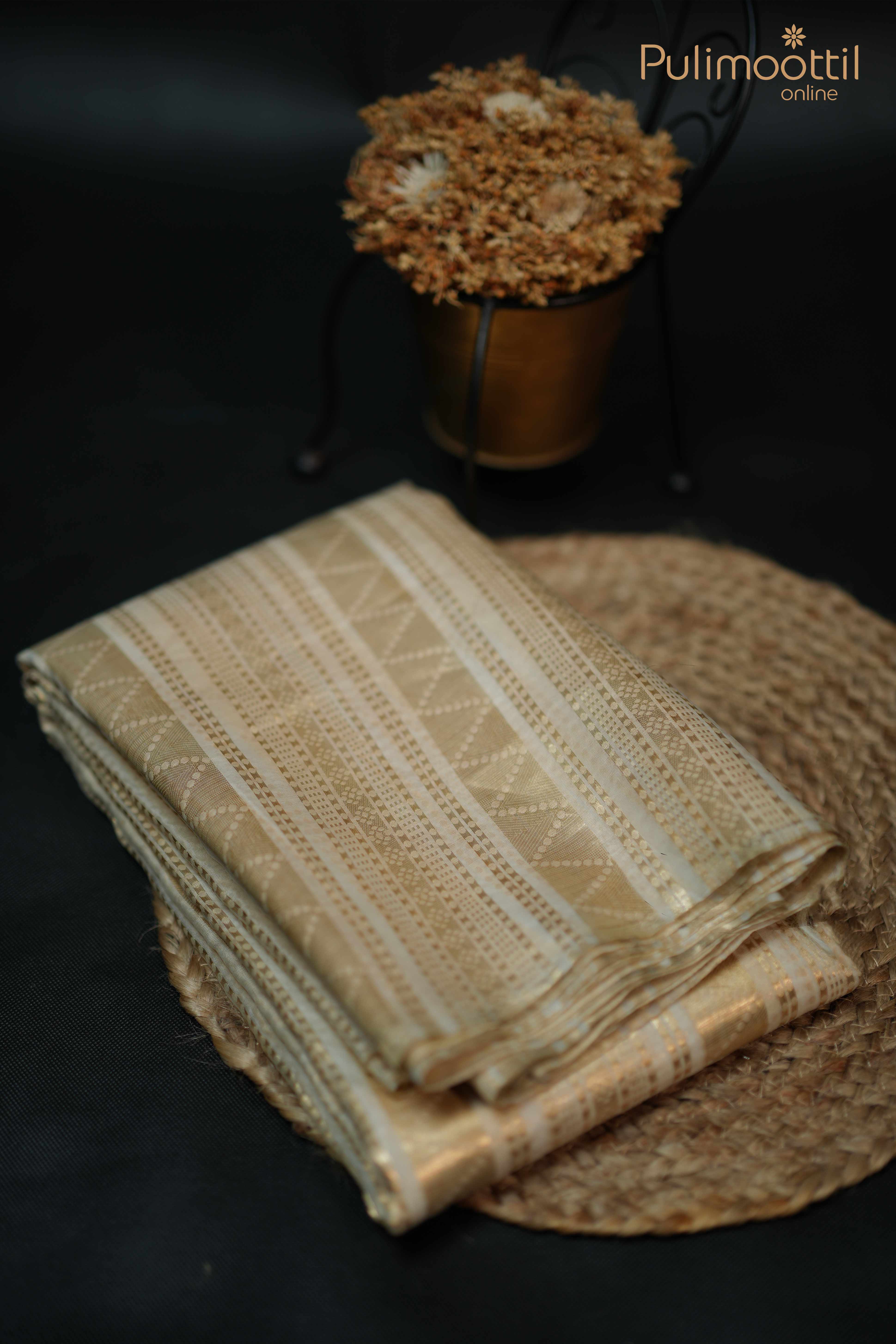 Folded cream organza saree with intricate golden zari patterns, placed on a jute mat for elegant product display.