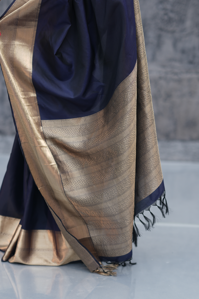 Detailed shot of the brocade pallu of an ink blue Kanchipuram silk saree featuring intricate golden zari weaving and traditional patterns.