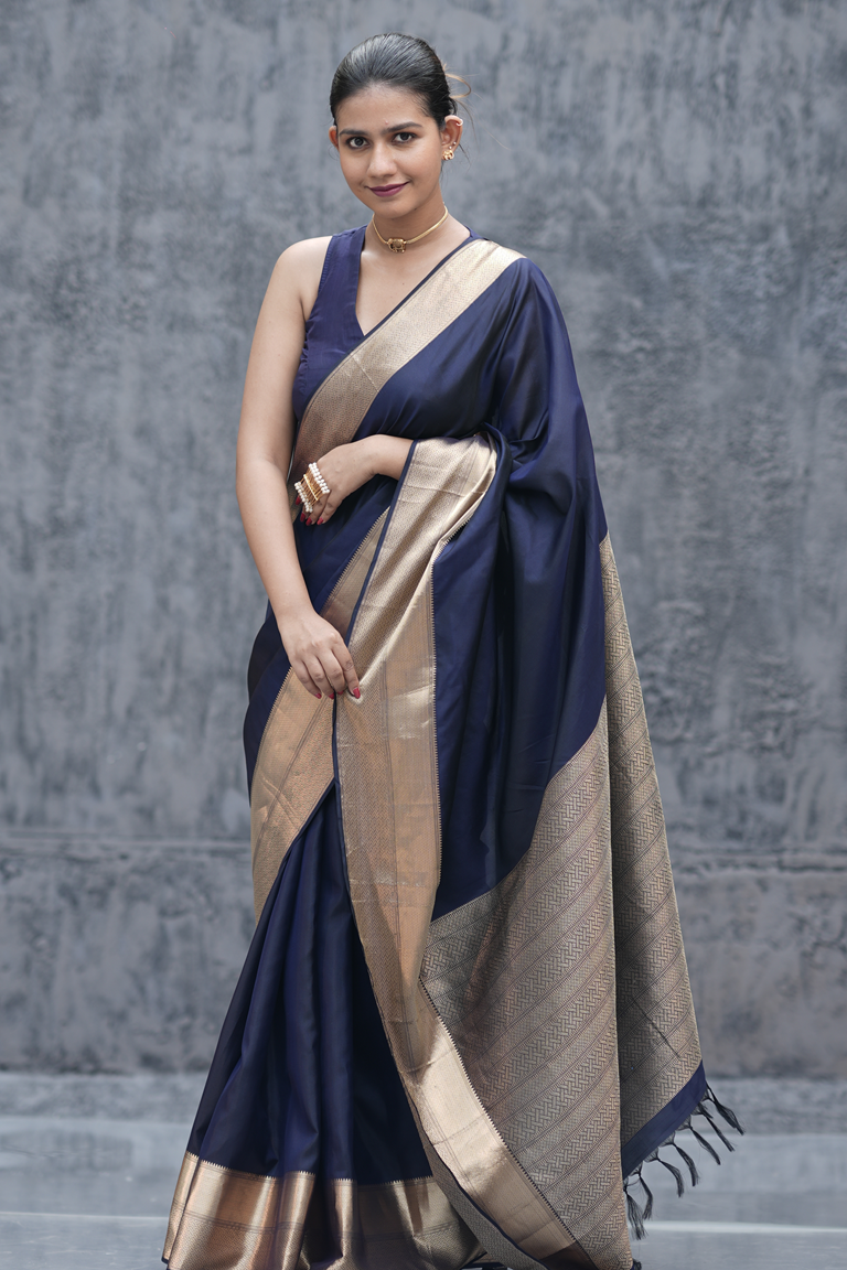Close-up of a woman wearing an ink blue Kanchipuram silk saree with a plain body and elegant golden zari double border, paired with a sleeveless blouse.
