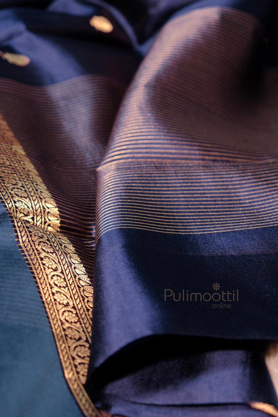 "Close-up of mango silk saree showcasing intricate golden zari border and fine horizontal zari lines on glossy blue fabric.