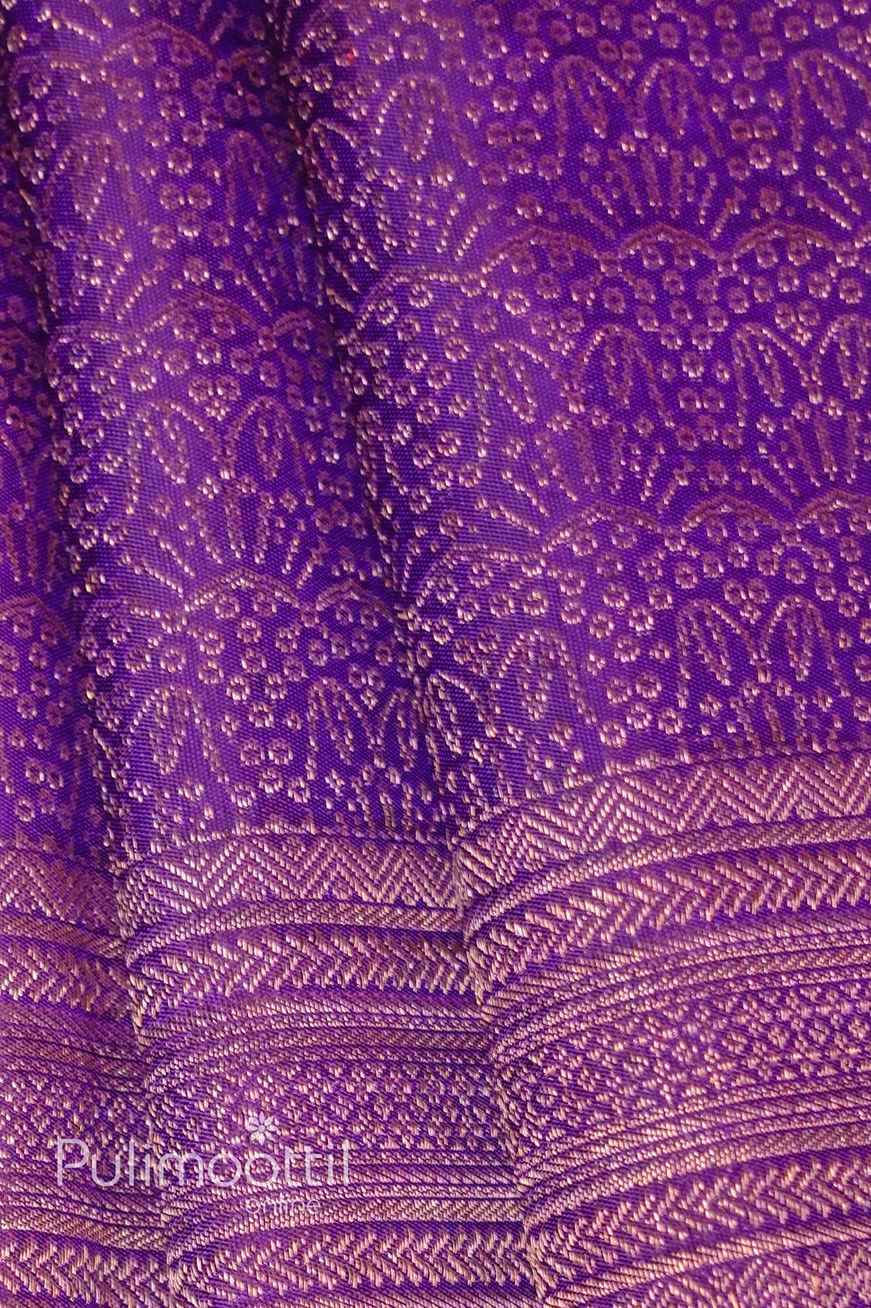 Macro view of dark purple Kanchipuram silk texture with gold-zari chevron weave and subtle sheen.
