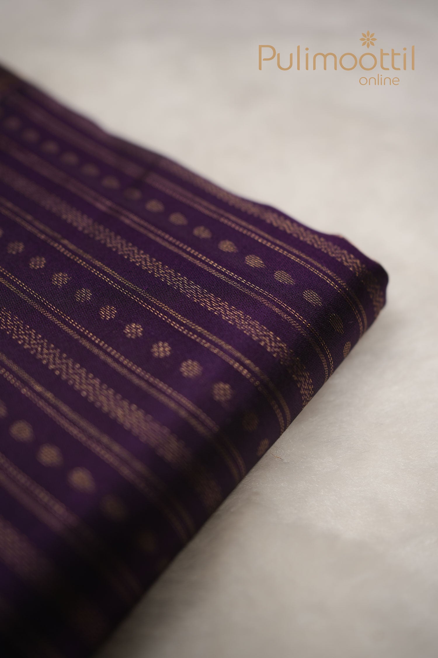 Dark purple Kanchipuram silk saree featuring fine golden zari stripes and scattered small buttas, draped to highlight the rich silk weave and border.