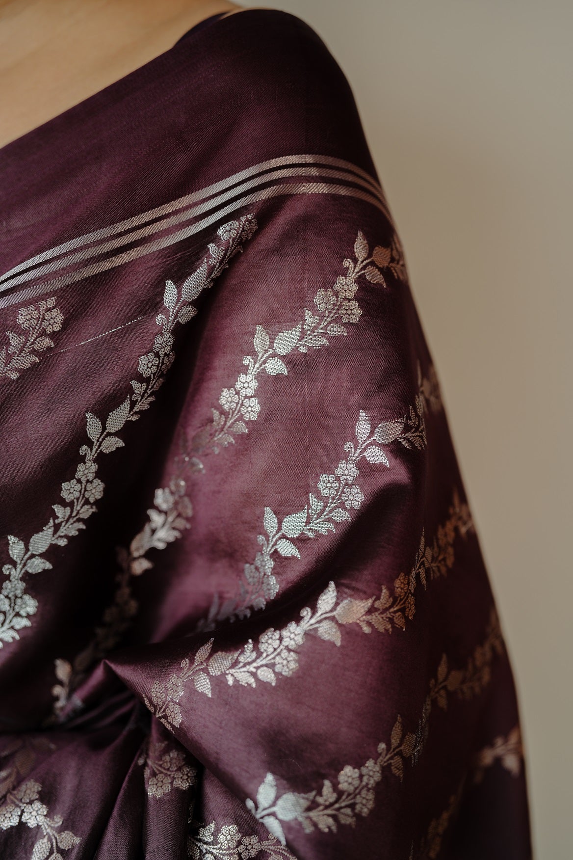 Close-up of deep coffee mango silk saree featuring silver and golden zari floral motifs on rich silk fabric.