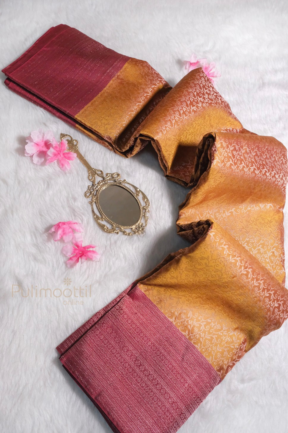 Handwoven silk saree in golden yellow with maroon border displayed with traditional mirror and pink flowers