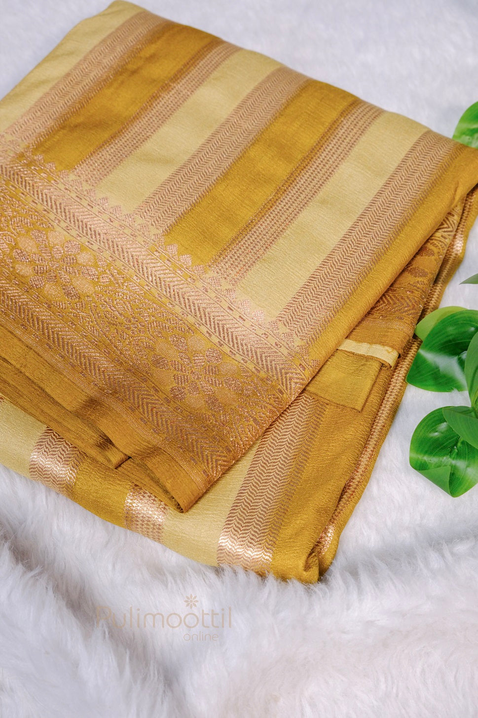 Golden silk saree folded on faux fur; broad jacquard border with mauve‑gold floral motifs and alternating stripe panels.
