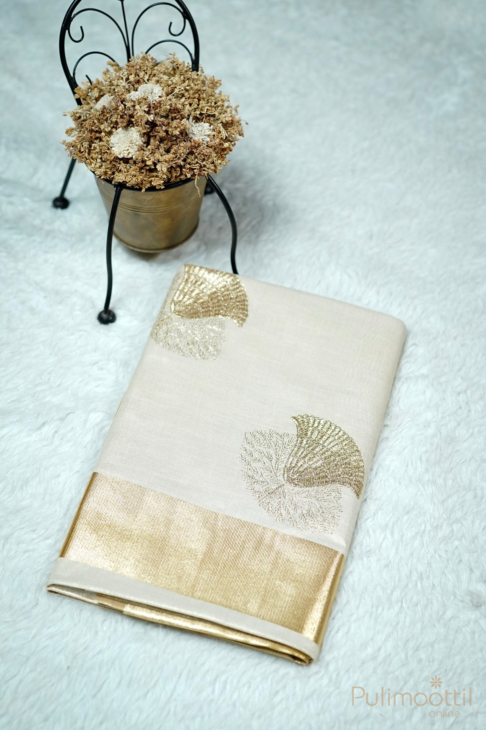 "Folded Kerala saree with golden tissue border and embroidery design on white fur with potted dried flowers