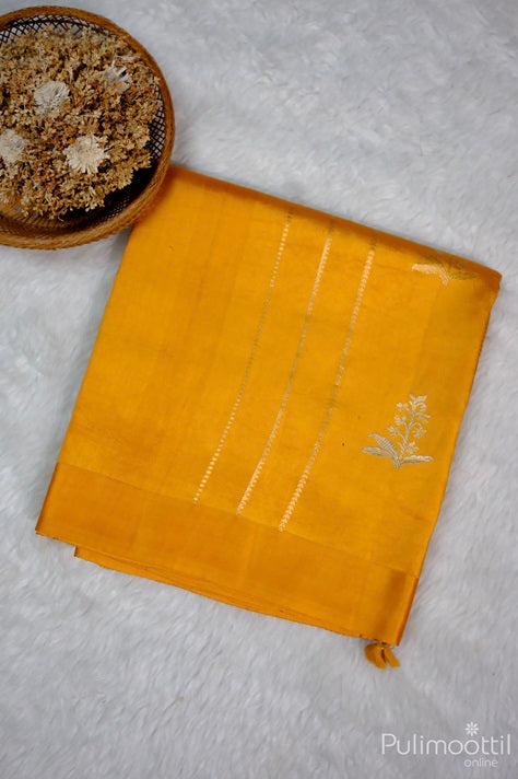 Folded Golden Yellow Mango Saree with Geometric Pattern Lines and Zari Floral Design, Surrounded by a Basket of Dried Flowers.