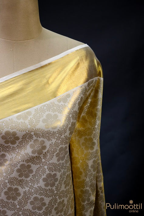 Kerala traditional brocade saree draped on mannequin, showing golden tissue pallu and floral woven body