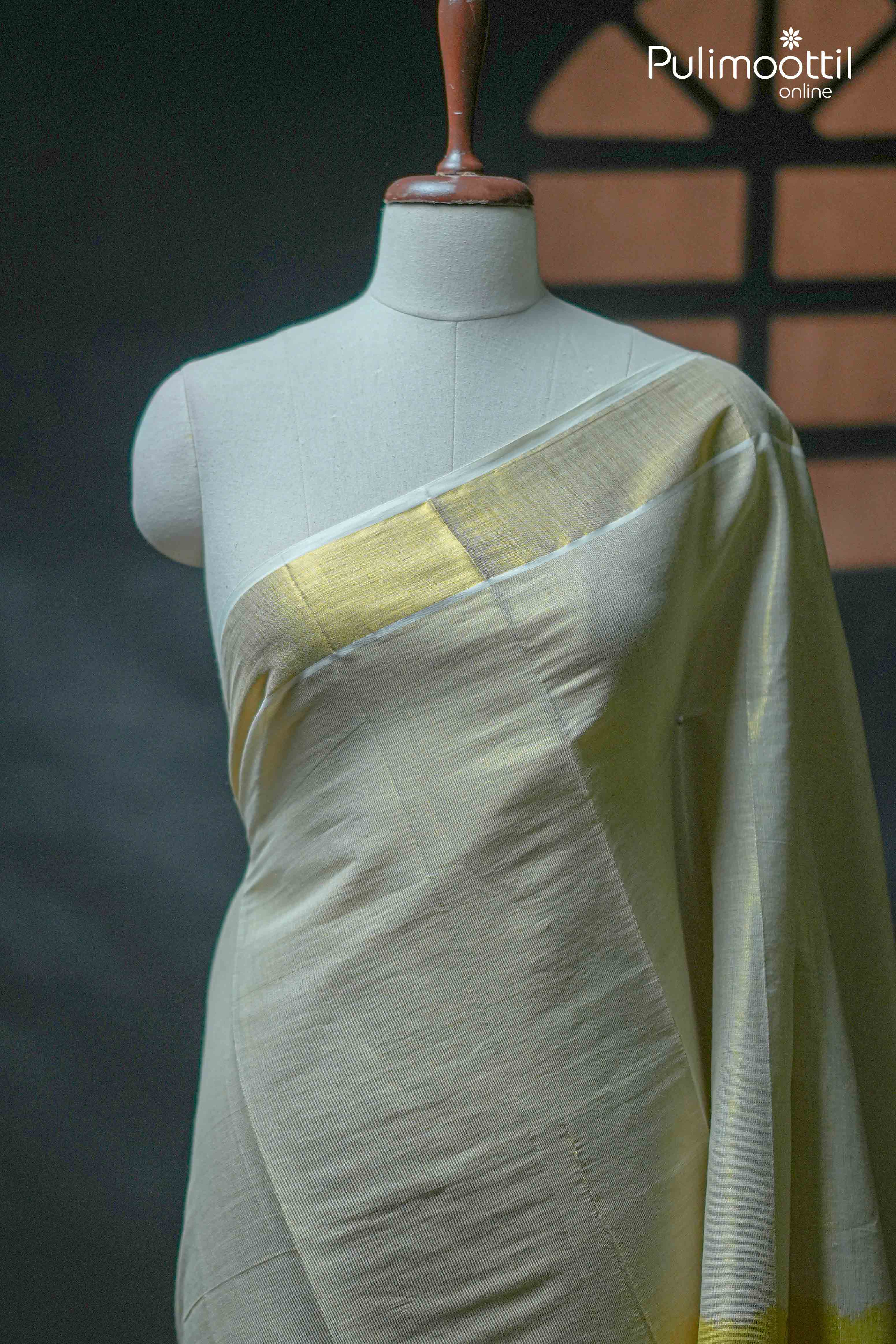 Kerala traditional golden tissue saree with half-and-half design and golden border, draped on mannequin in soft lighting.