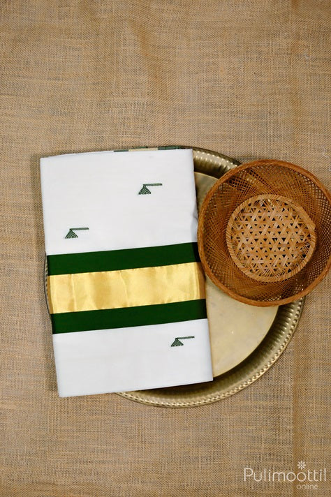 Folded Kerala traditional handloom set saree in off-white with green thread motifs and golden tissue border, placed on a brass plate over jute fabric – perfect for Onam gifting or festive wear.

