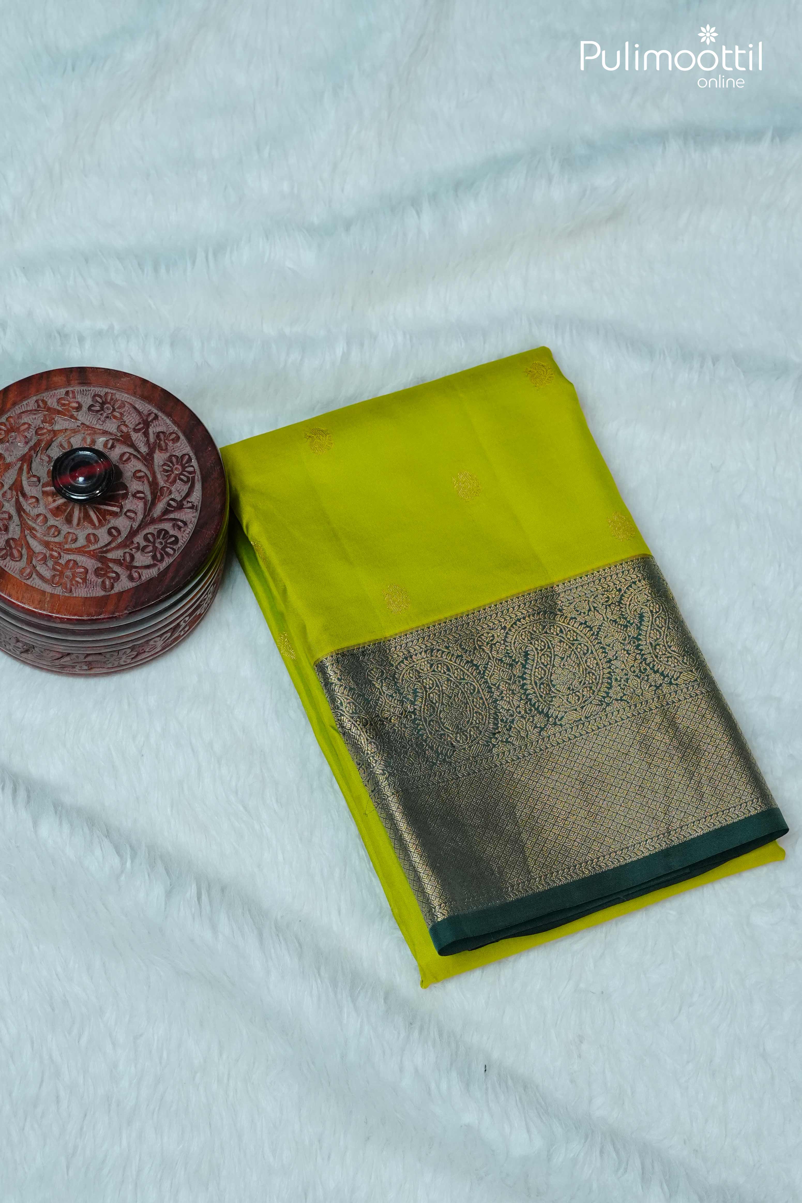 Folded lime green Kanchipuram silk saree with golden zari peacock motifs and contrast green border placed on white background
