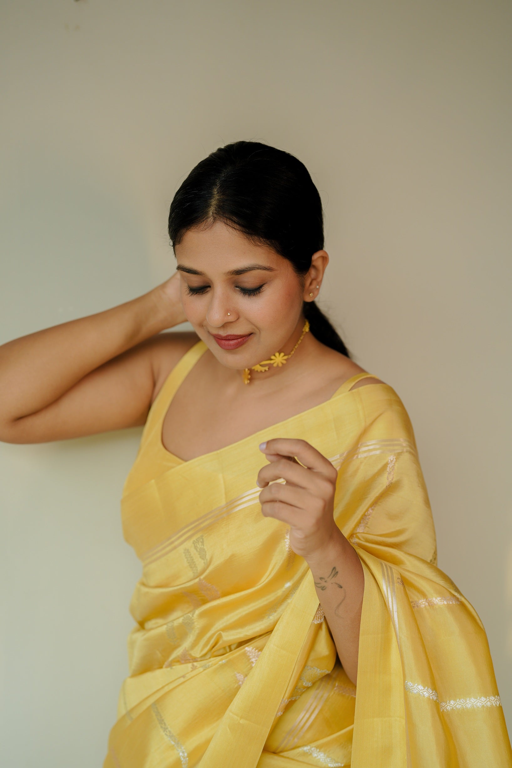 Close-up of a woman wearing a yellow mango silk saree with silver zari stripes, posing gracefully with a hand behind her head.
