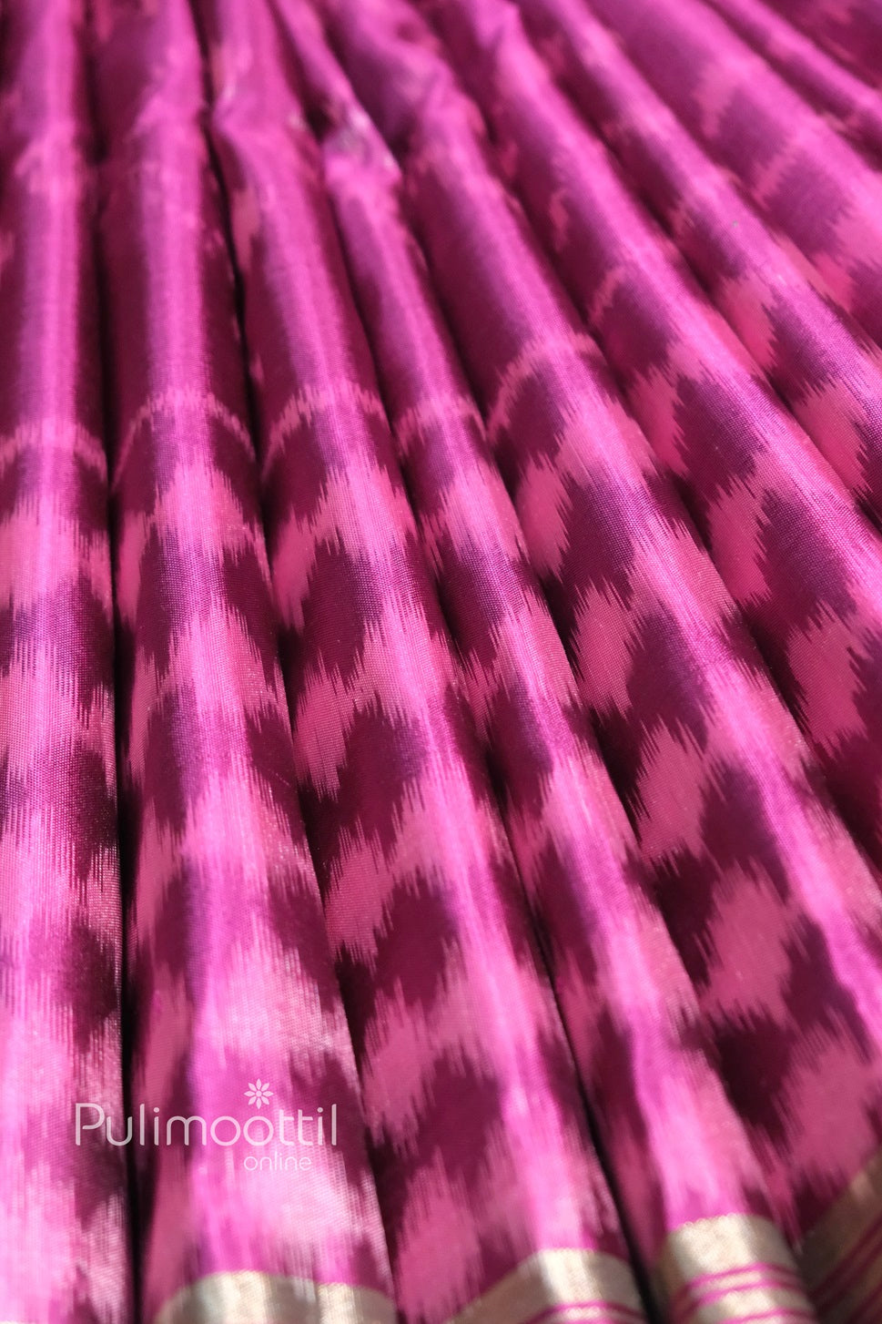 Pleated view of magenta soft silk saree featuring vibrant ikkat pattern in pink and purple shades with subtle antique zari border.