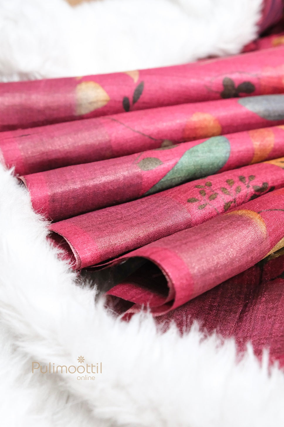 Close-up of Pure Jute Silk Saree in deep pink with elegant multicolor floral design, showcasing the soft texture and natural sheen of the fabric, laid on white faux fur background.