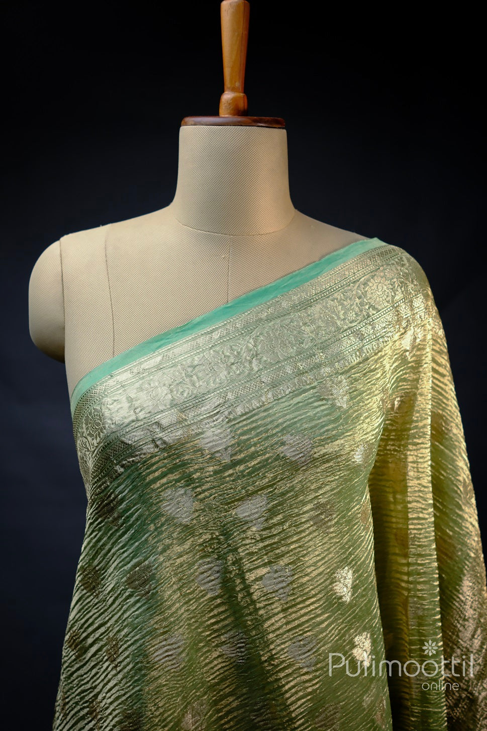 Mint green crushed Banarasi silk saree draped on a mannequin, featuring a light golden zari floral creeper design border, showcasing the elegant texture and intricate details of the fabric