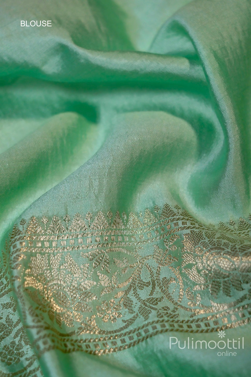Close-up of mint green fabric with a delicate gold zari floral border, showcasing the luxurious texture and intricate floral patterns along the edge, designed for a blouse.