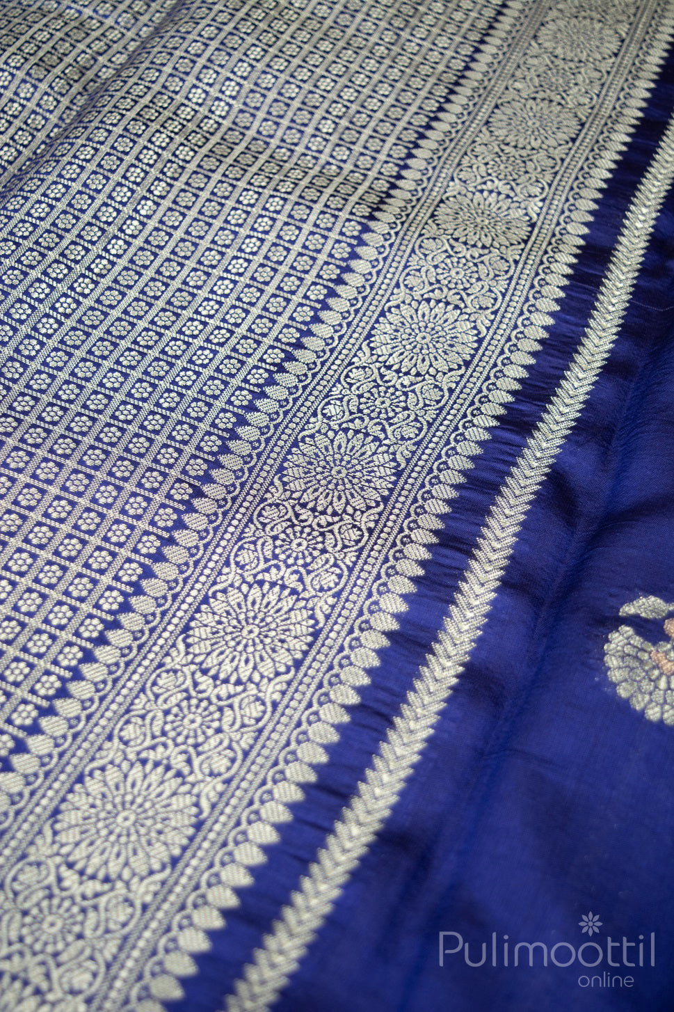 Close-up of intricate brocade-style pallu in navy blue Banarasi silk saree with rich gold and silver zari floral motifs and traditional woven texture.